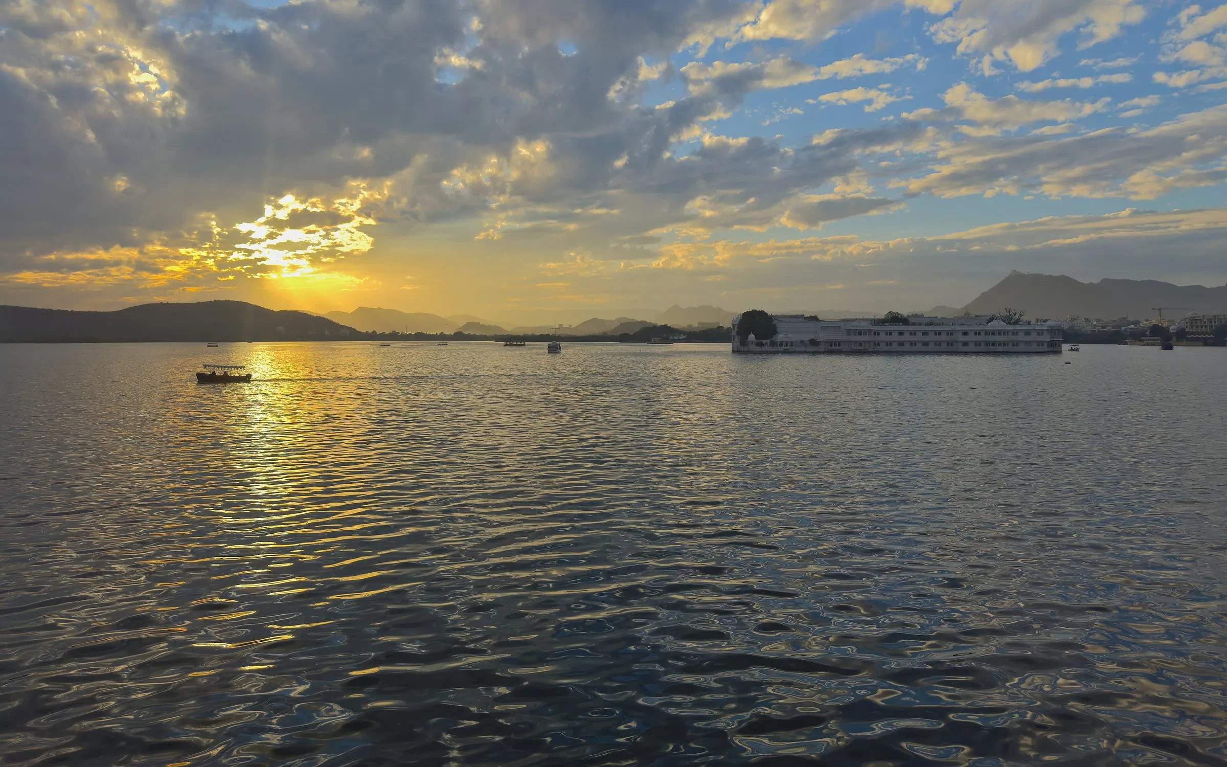 Le lac Pichola au coucher du soleil à Udaipur, palais et collines à l’horizon